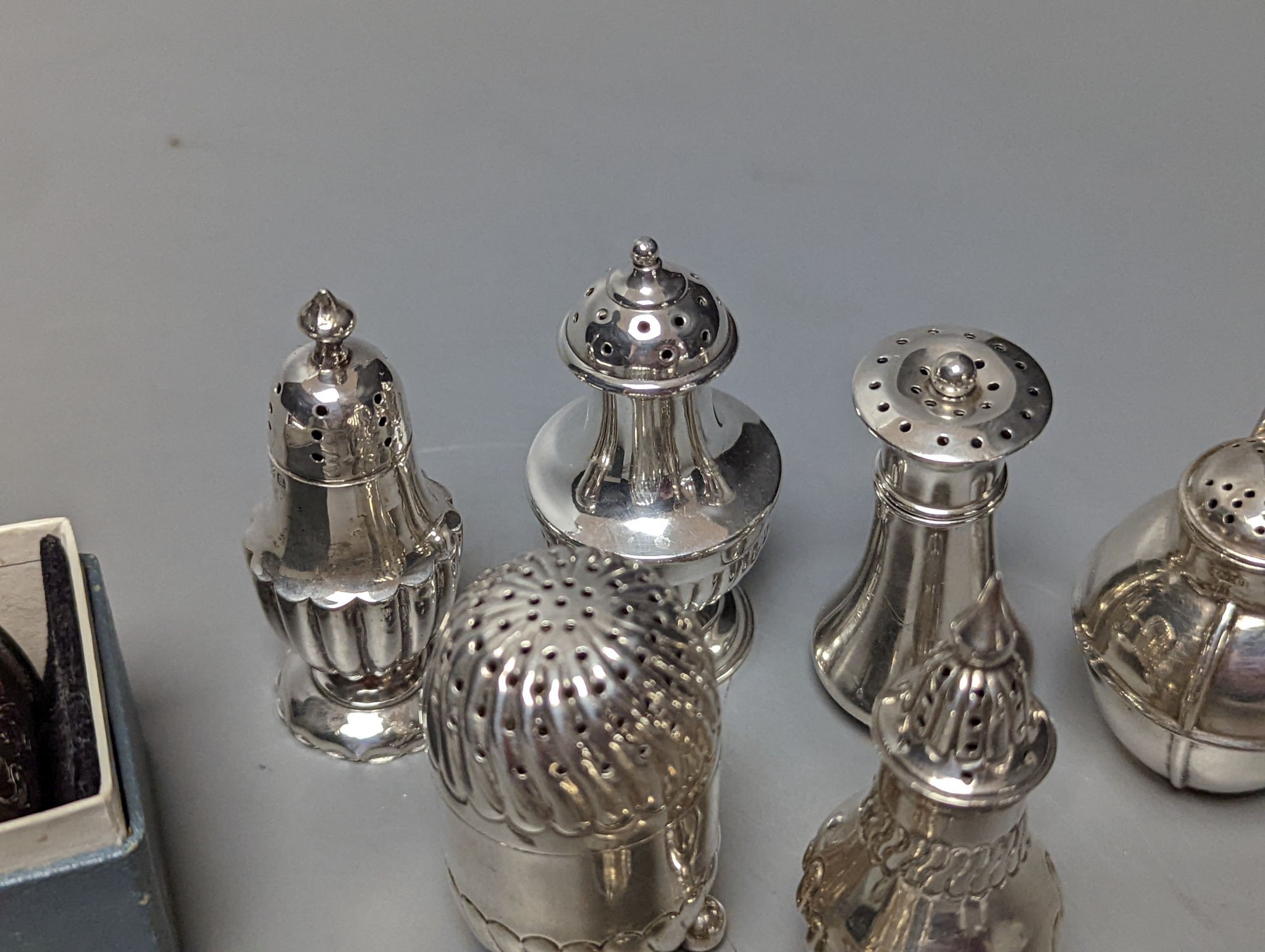A cased silver napkin ring, seven assorted silver pepperettes including Guernsey can and a pair of plated sugar tongs.